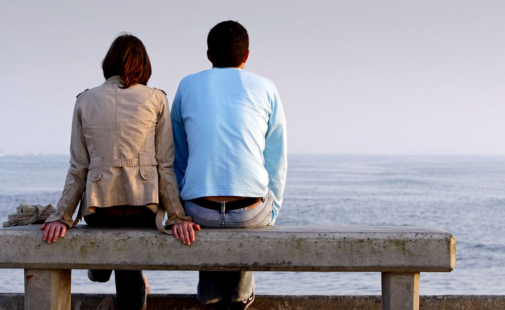 Couple sits on bench at ocean after committing to each other
